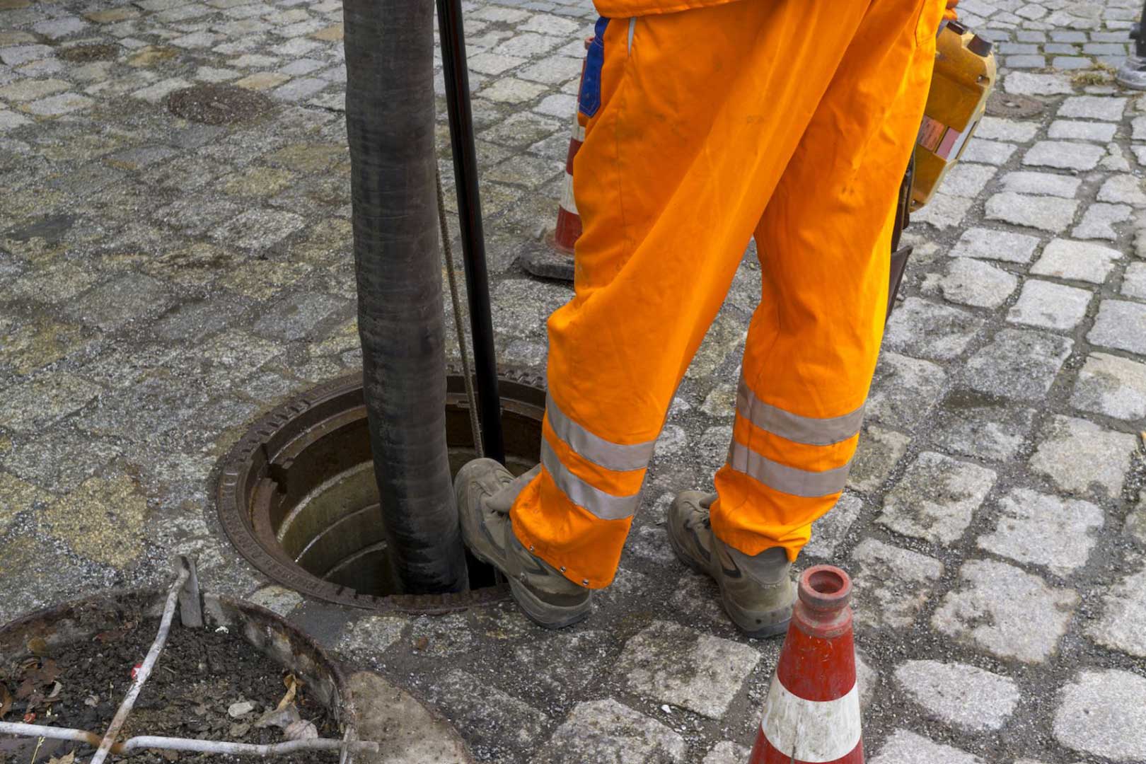 Sewerage worker on cobblestone street cleaning manhole with hydrovac