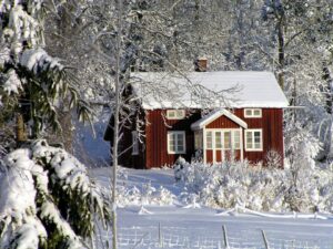 Red-brick-home-with-snow-covered-roof-in-front-of-a-forest-in-winter