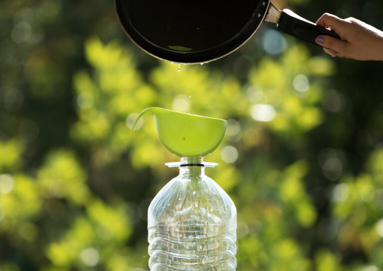 skillet pouring grease into a green funnel placed over plastic water bottle
