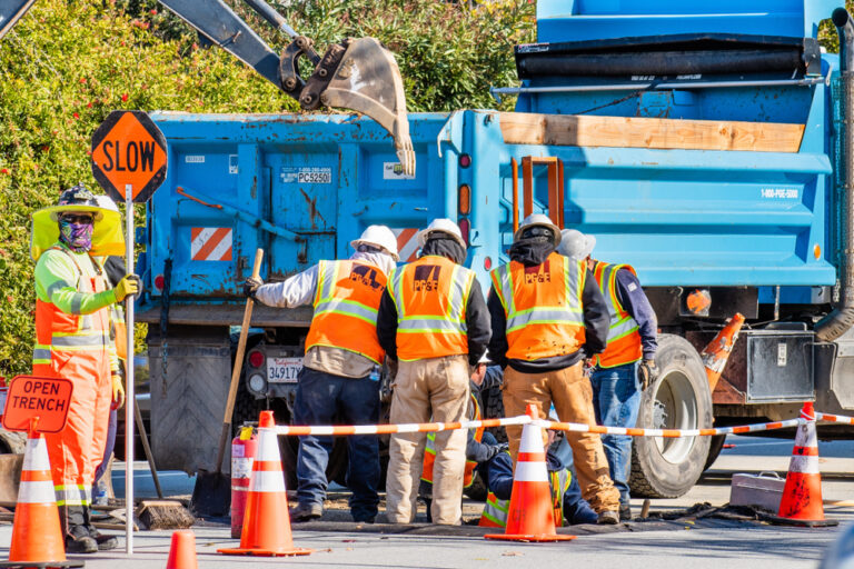 group of construction workers in orange vests stand in front of blue dump truck