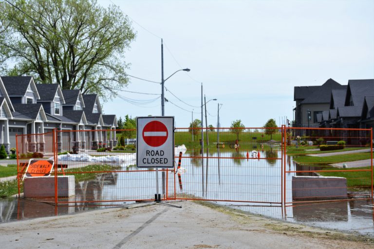 Road closed sign on orange fencing blocking off flooded road