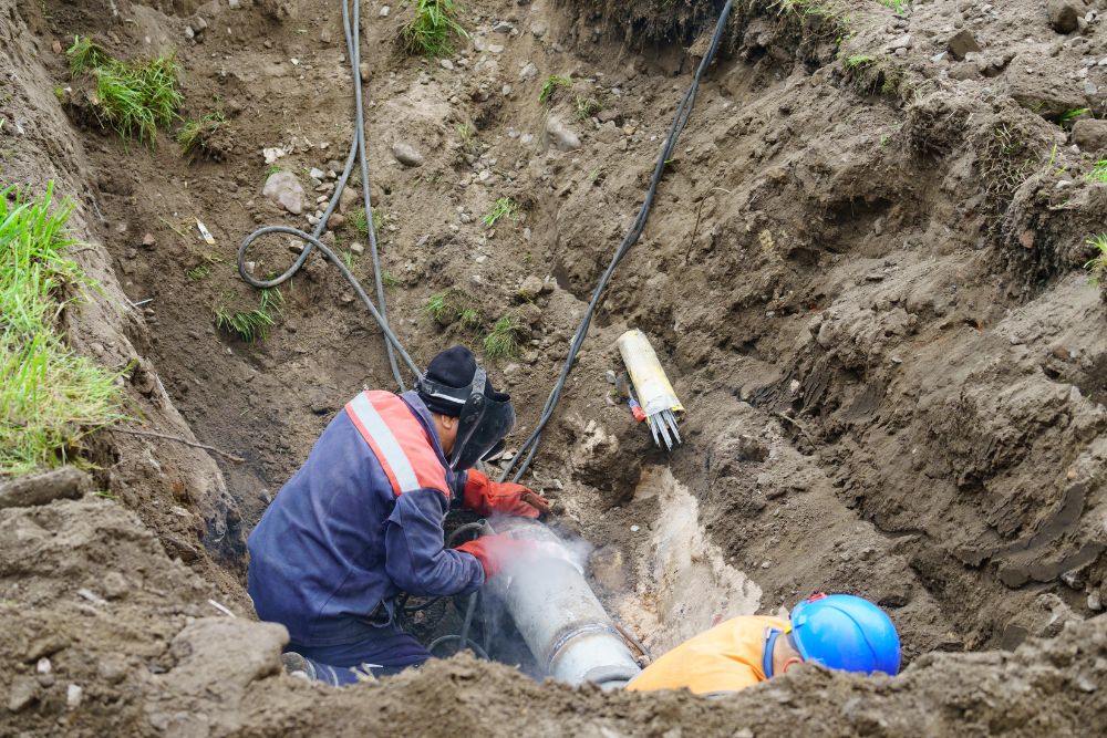 technician fixes sewer line in trench