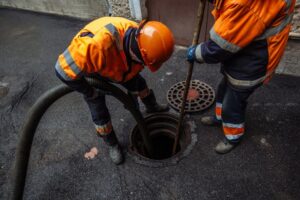 Utility workers servicing a sewer manhole with industrial equipment