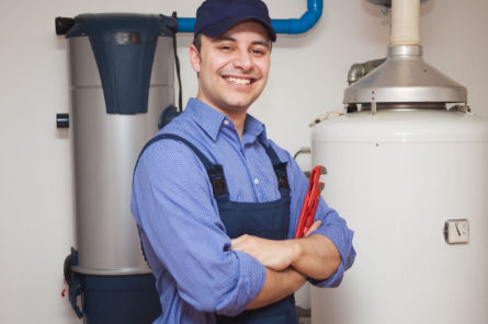 Professional plumber smiling beside water heater and plumbing system during sewer line inspection.