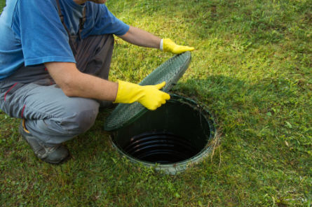 Worker lifting a septic tank access cover for inspection and maintenance – Peak Sewer septic system services.