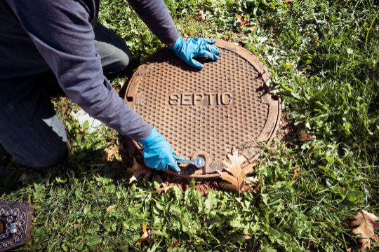 Technician opening a septic tank lid during inspection on a residential property – Peak Sewer septic system repair services.