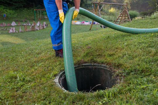 Technician pumping out a residential septic tank with a large hose as part of septic system maintenance by Peak Sewer.