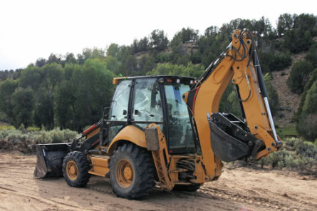 Yellow backhoe excavator on a construction site used by Peak Sewer for septic system installation and utility trenching.