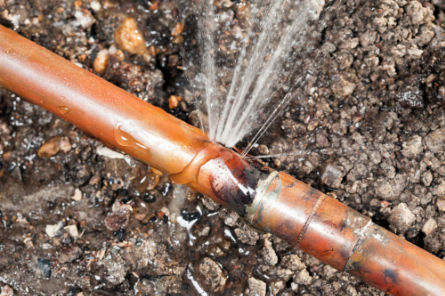 Close-up of a leaking underground copper pipe being repaired after a blockage and pressure buildup.