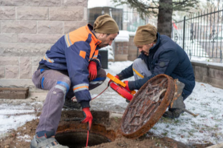 Two technicians opening a manhole and conducting a sewer line camera inspection in winter conditions.