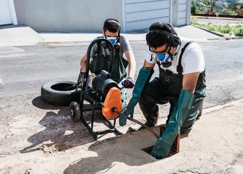 Two technicians using professional equipment to clean and unclog a street drain, part of Peak Sewer’s drain steam cleaning service.