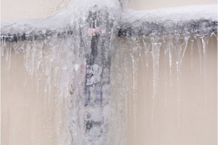 Frozen exterior pipe encased in thick ice and icicles, showing winter conditions that may require steam thawing services.