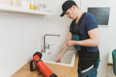 Drain cleaning technician snaking a kitchen sink to remove a clog as part of professional drain cleaning services.