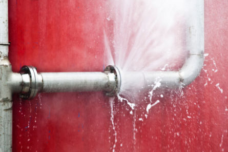 High-pressure water spraying from a damaged metal pipe, showing the need for professional drain and pipe maintenance.