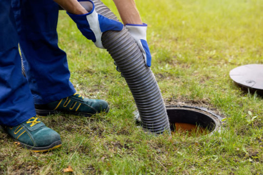 Technician using a large suction hose to clean an outdoor drain or septic access point on a lawn.