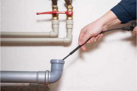 Technician inserting a camera or steam hose into a drain pipe for inspection or thawing service.