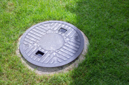 Septic tank cover installed flush with grass lawn, part of a modern septic system design by Peak Sewer.