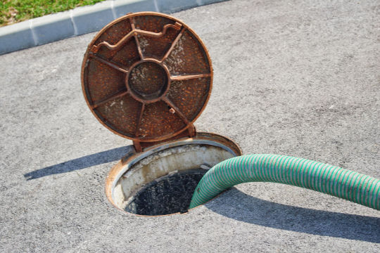 Septic tank pumping in progress with hose connected through open access lid, performed by Peak Sewer.