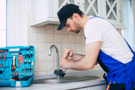 Plumber using a plunger to clear a kitchen sink drain as part of Peak Sewer’s residential drain cleaning service.