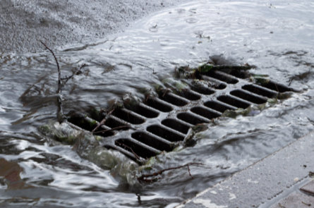 Storm drain intake with heavy water flow, showing drainage systems that may require flushing or hydrovac cleaning.