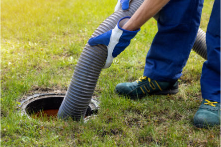 Worker using a large vacuum hose to clean a sewer or septic tank through an outdoor access point on a grassy lawn in Edmonton.